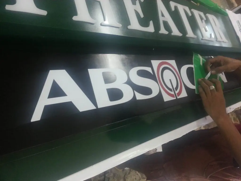 ABS-CBN theater signboard signage, Makati—hands apply green sticker above logo and text. Signage by M&G Global Ads.