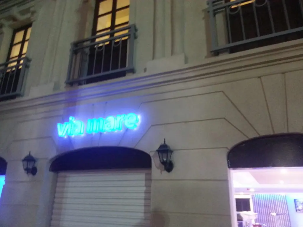 Neon blue signage for Via Mare above a building facade in Makati at night, with balconies, by M&G Global Ads.