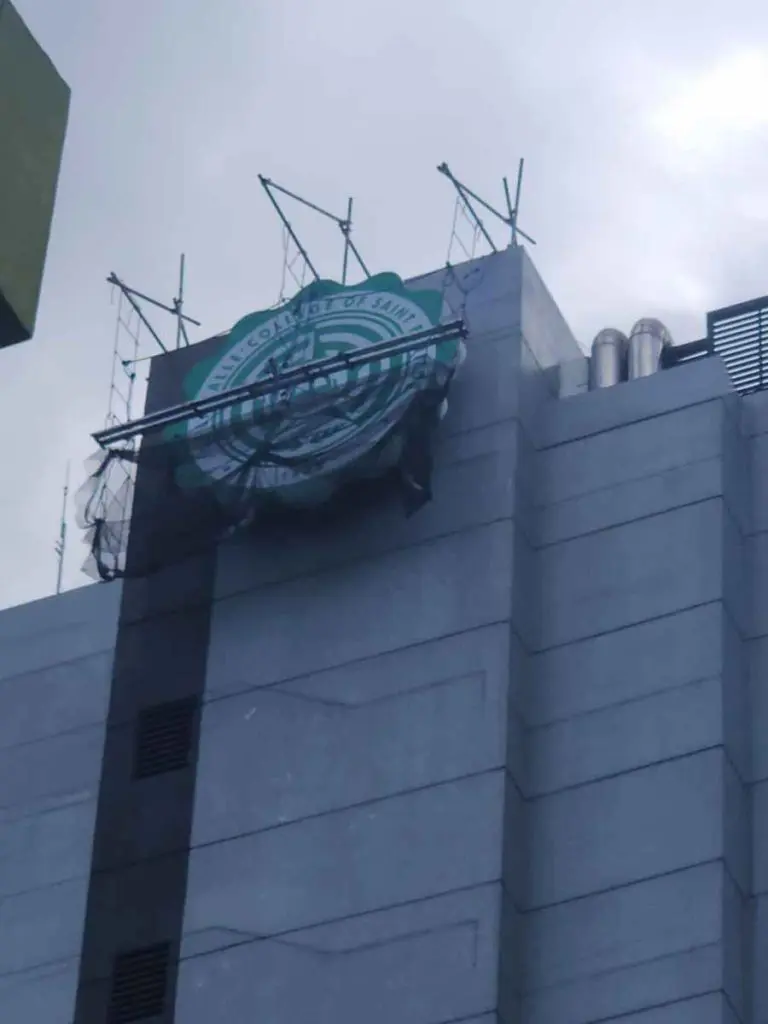 Damaged Starbucks Coffee outdoor signage on tall gray building in Makati with exposed metal supports. by M&G Global Ads.