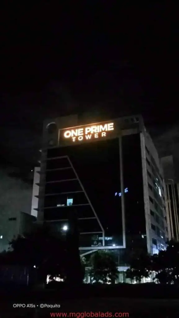 ONE PRIME TOWER LED signage at night in BGC, illuminated at the top with surrounding lights and trees, by M&G Global Ads.
