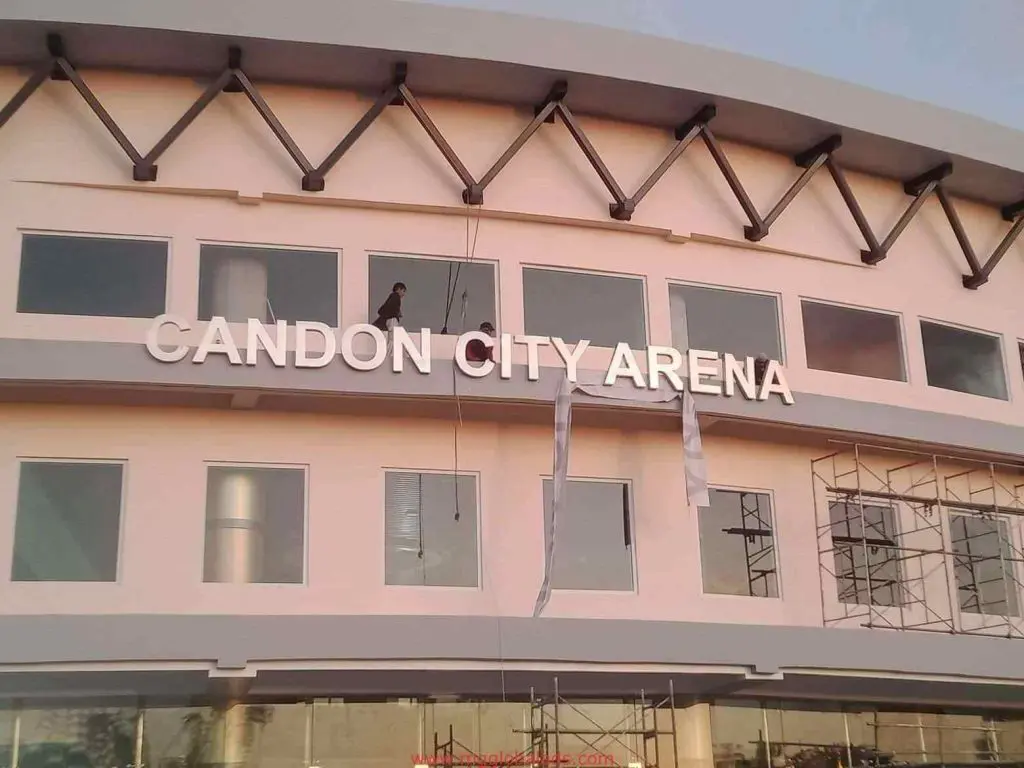 Candon City Arena building signage with large white letters in Makati, workers and scaffolding visible, by M&G Global Ads.