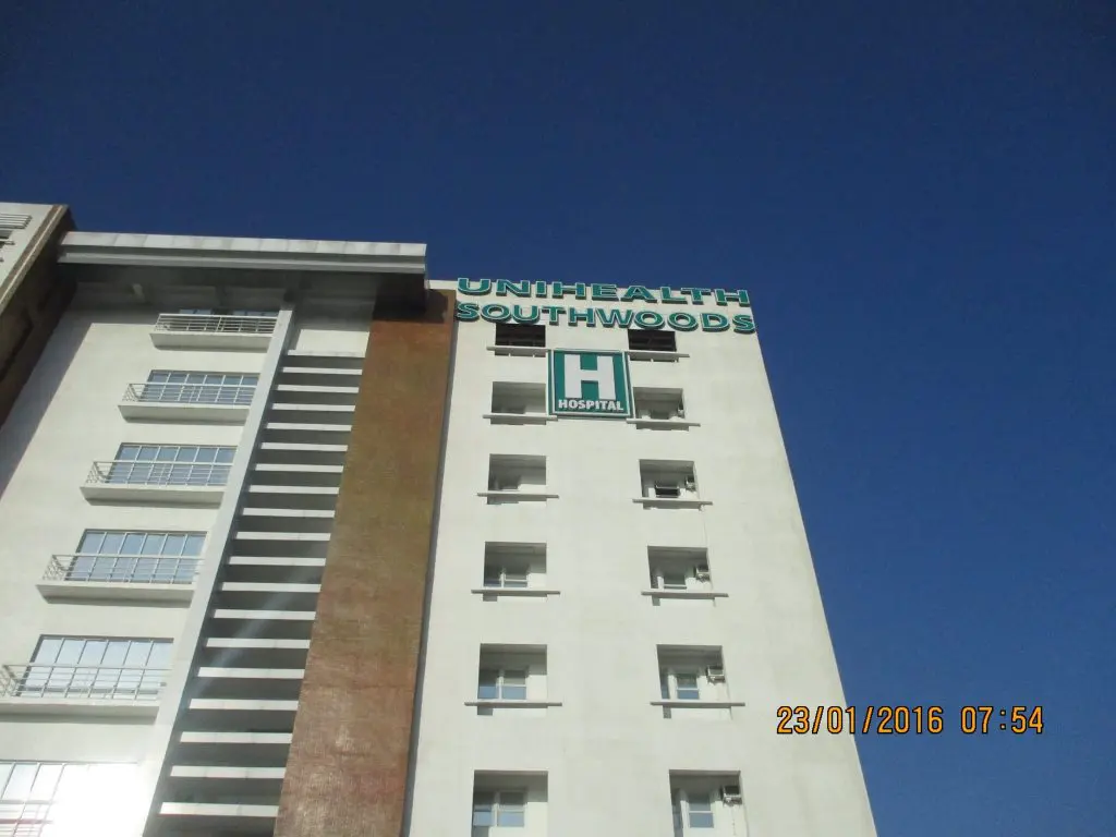 UNIHEALTH SOUTHWOODS hospital exterior with green hospital signage in Makati, clear sky, by M&G Global Ads.