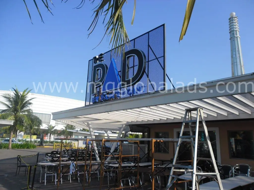 Blue and black pylon signage installation for PD on a rooftop in Quezon City by M&G Global Ads, workers and palm trees visible.