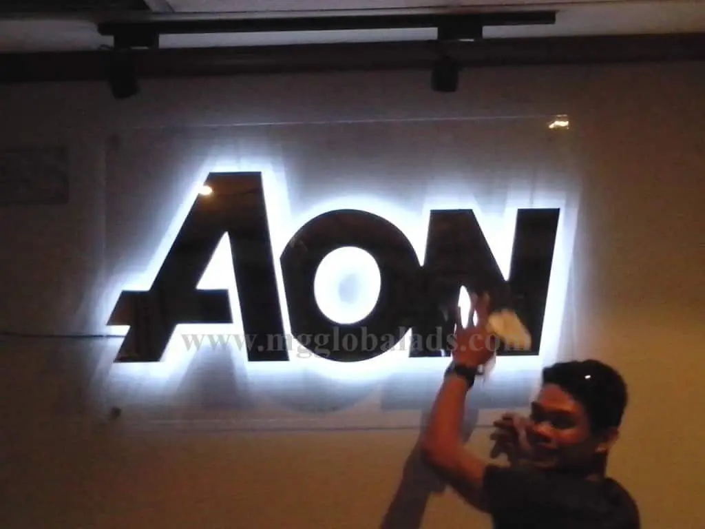 AON indoor LED signage in Makati, person smiling and pointing at the bright display; dim background. By M&G Global Ads.