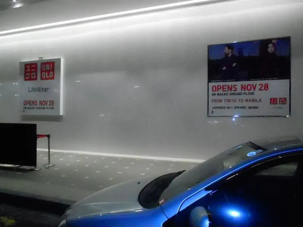 UNIQLO building signage and posters at SM Makati for store opening, well-lit exterior, blue car in front, by M&G Global Ads.