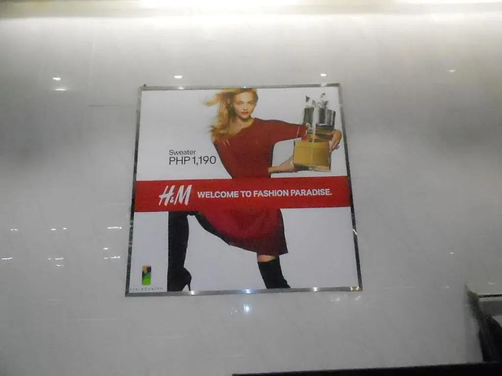 H&M outdoor poster signage in Quezon City, model in red sweater with shopping bags, promo details visible by M&G Global Ads.