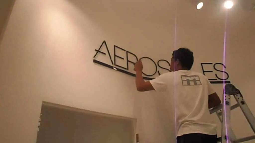 Installing black acrylic AEROS signage on white wall in Makati, under spotlights, by M&G Global Ads.