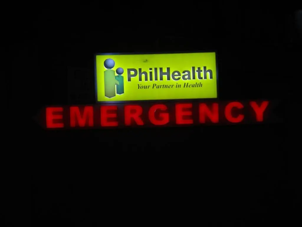 Lit acrylic emergency signage for PhilHealth with logo and red arrow in Quezon City healthcare facility by M&G Global Ads.