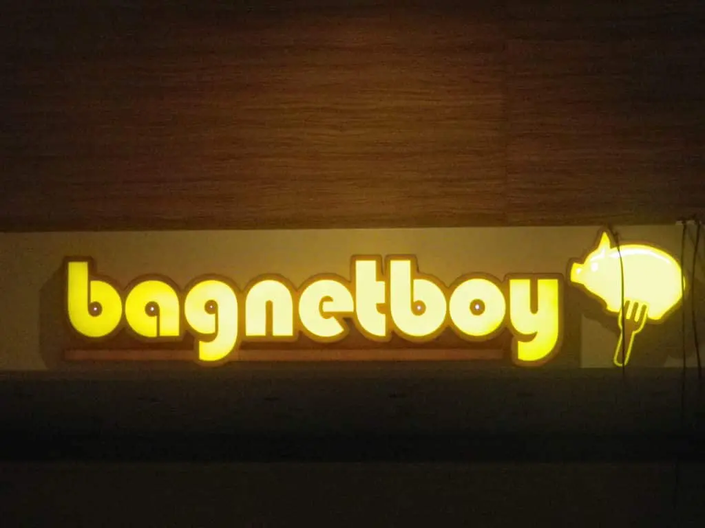 Glowing yellow outdoor building signage for Bagnetboy with pig on fork, wood background, Makati location by M&G Global Ads.