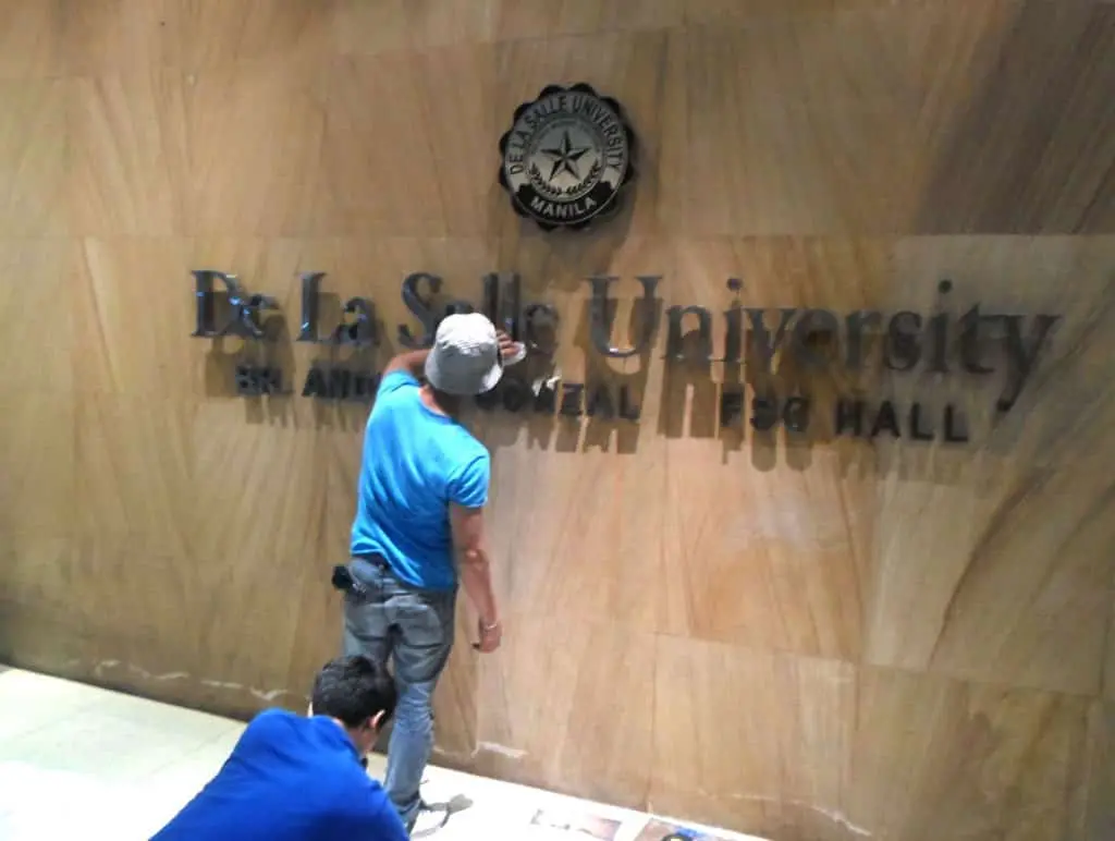 Indoor signage installation for De La Salle University by M&G Global Ads in Mandaluyong; two workers at Br. Andrew Gonzalez FSC Hall.