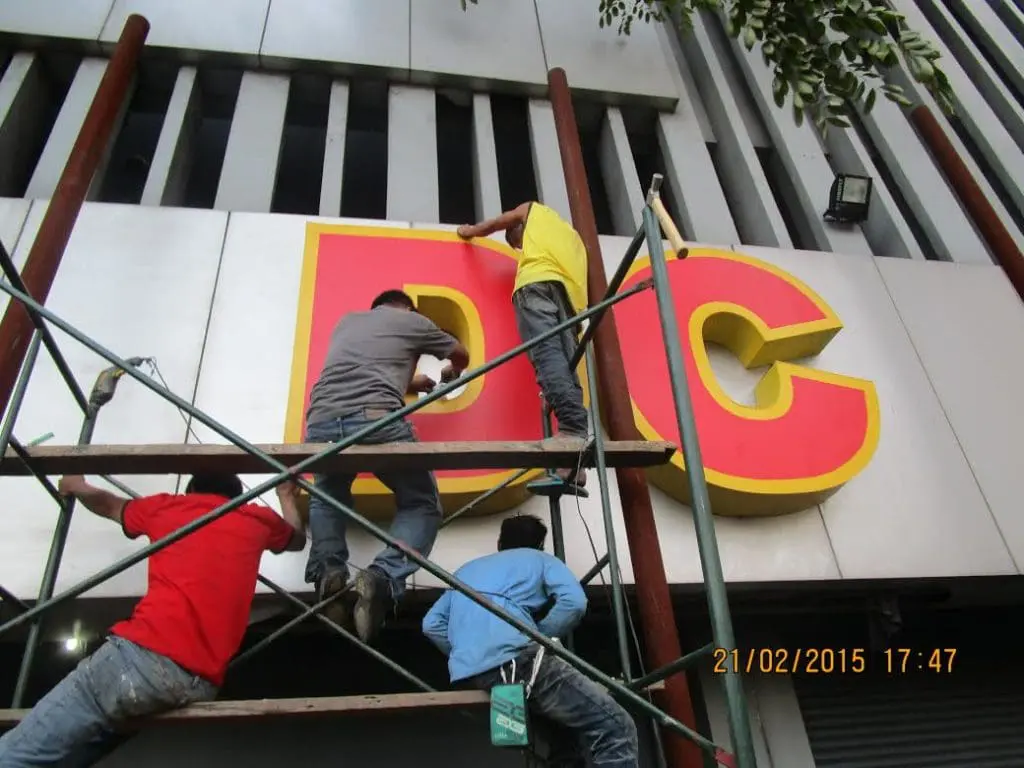 Channel letter signage installation in Makati, large D and C letters on facade, four workers on scaffolding by M&G Global Ads.