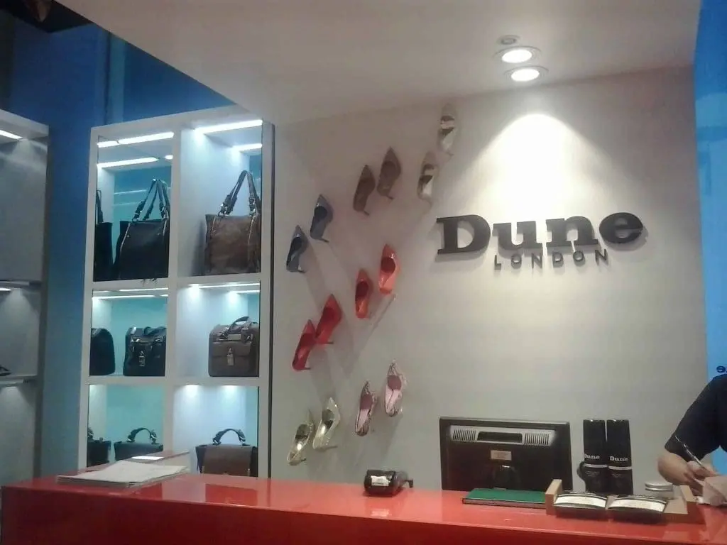 Acrylic Dune London signage at store counter in Makati with decorative shoes and handbags, by M&G Global Ads.