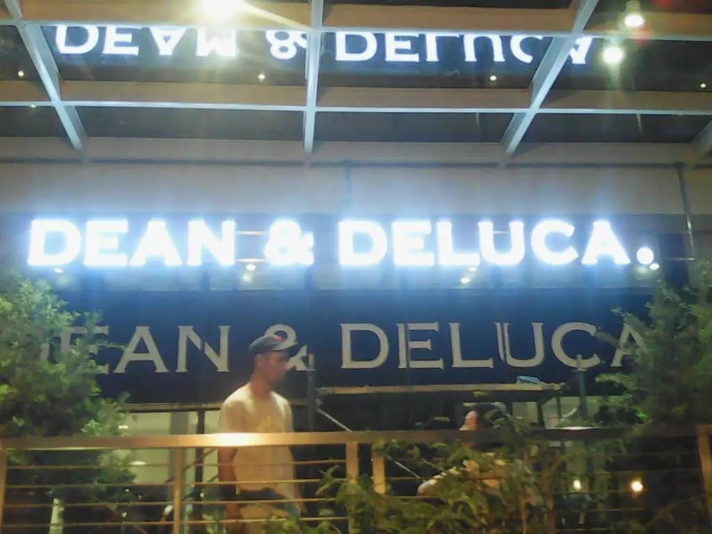 DEAN & DELUCA lighted storefront signage with green plants, reflections, at night in BGC by M&G Global Ads.