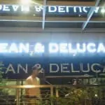 DEAN & DELUCA lighted storefront signage with green plants, reflections, at night in BGC by M&G Global Ads.