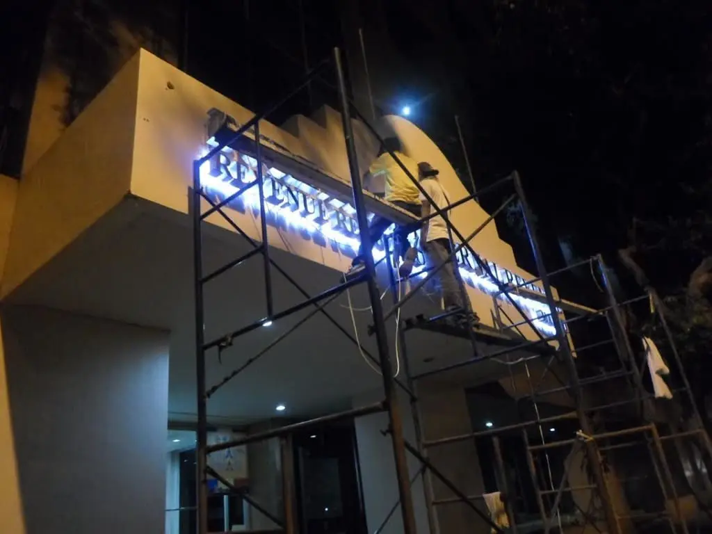 Acrylic signage installation and repair at a building entrance in Makati at night, illuminated by lights, by M&G Global Ads.
