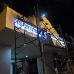Acrylic signage installation and repair at a building entrance in Makati at night, illuminated by lights, by M&G Global Ads.