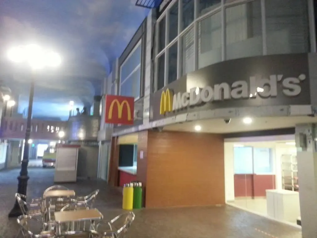 McDonalds lighted building signage in Quezon City indoor branch, with empty tables, lamp post, and bins. By M&G Global Ads.