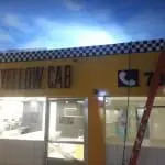 Yellow Cab lighted storefront signage with checkered design in Makati, red ladder nearby, by M&G Global Ads.
