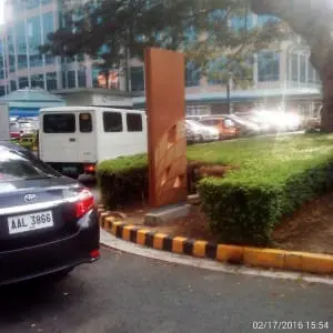Brown acrylic office signage in front of a building with cars and landscaping, Makati. Signage by M&G Global Ads.