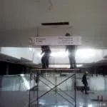 Workers install mall wayfinding signage on scaffolding in Makatis unfinished site with ceiling gaps. By M&G Global Ads.