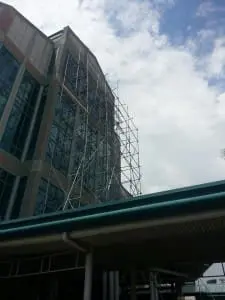 Outdoor pylon signage at a tall glass building with scaffolding in Makati, covered walkway in front by M&G Global Ads.