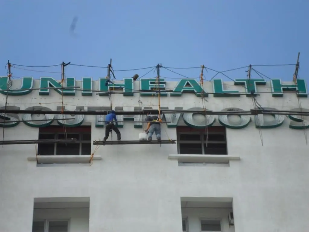 Outdoor LED signage for UNIHEALTH SOUTHWOODS in Quezon City, cleaned by workers on ropes. By M&G Global Ads.