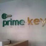 Acrylic indoor signage for Prime Key in green and gold on a white brick wall, Makati office reception by M&G Global Ads.