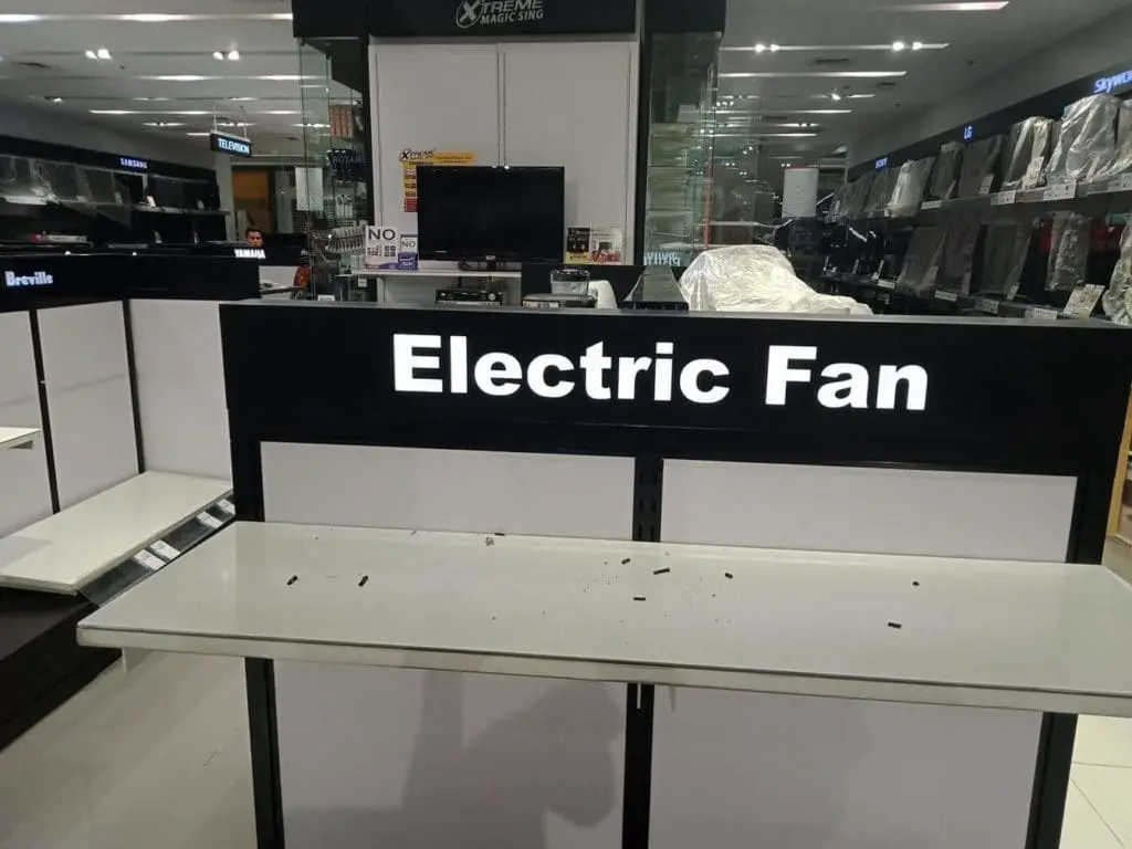 Acrylic signage display for Electric Fan on empty store shelves and table in Makati, some debris visible. By M&G Global Ads.
