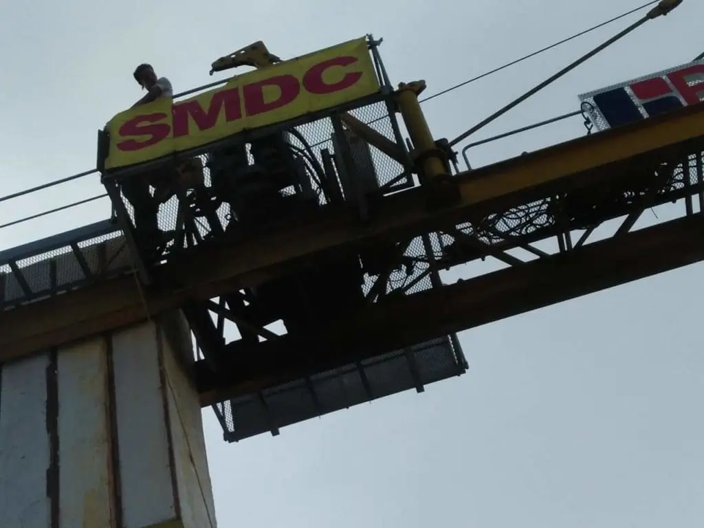 Outdoor billboard signage for SMDC displayed on a yellow crane in Ortigas. Overcast sky. Installation by M&G Global Ads.