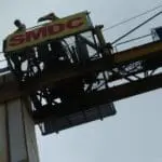 Outdoor billboard signage for SMDC displayed on a yellow crane in Ortigas. Overcast sky. Installation by M&G Global Ads.