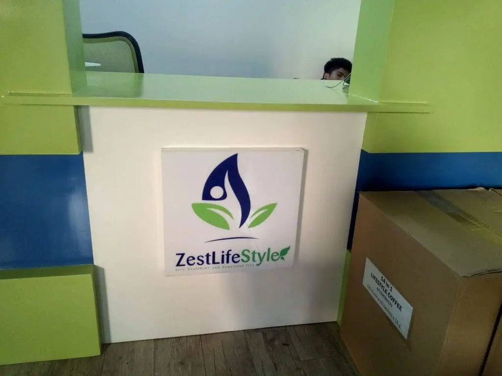 Acrylic signage for ZestLifeStyle at reception desk in Makati, with logo and partial staff behind desk by M&G Global Ads.