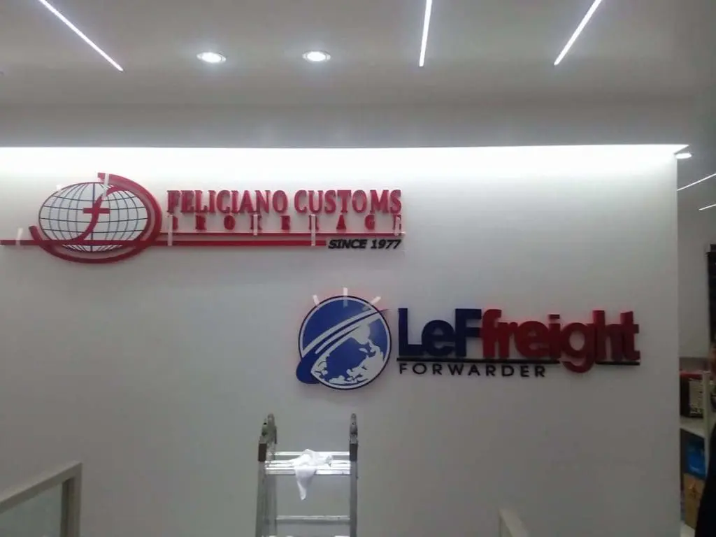 Metallic office signage for Feliciano Customs Brokerage and LeFreight Forwarder in Quezon City by M&G Global Ads. Ladder visible.