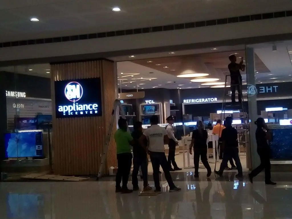 SM Appliance Center indoor signage installation in Quezon City mall entrance with workers and appliances, by M&G Global Ads.