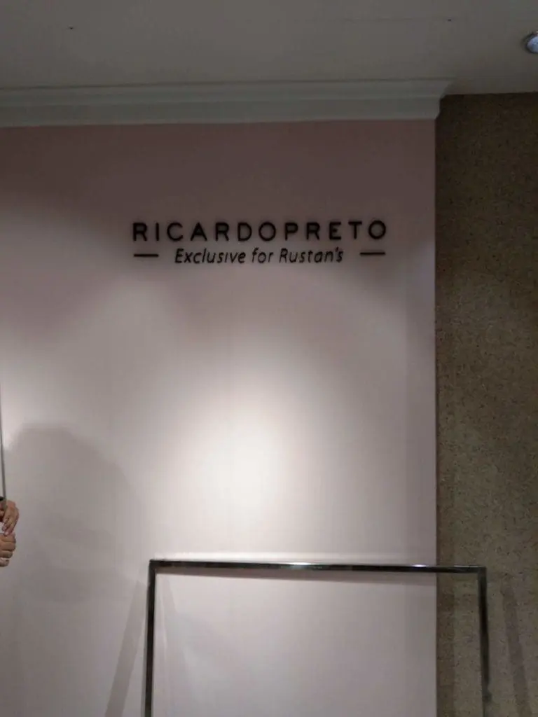 Black metallic indoor signage for Rustan’s on a pink wall in Makati, above a metal clothing rack. by M&G Global Ads.