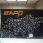 Acrylic signage with yellow APG logo and silver dots behind a white desk in Makati office, by M&G Global Ads.