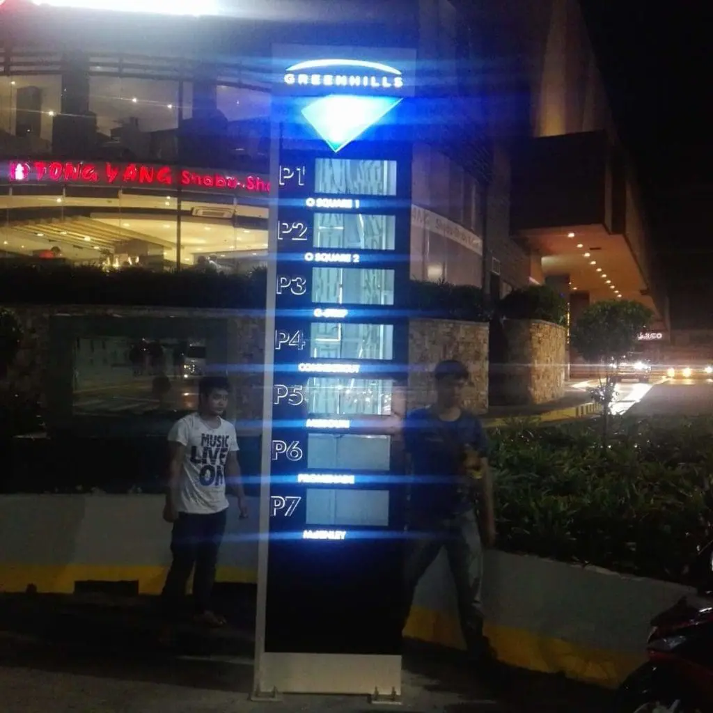 LED signage directory at Greenhills in San Juan shows parking levels P1–P7 and zones; people nearby, restaurant behind. by M&G Global Ads.