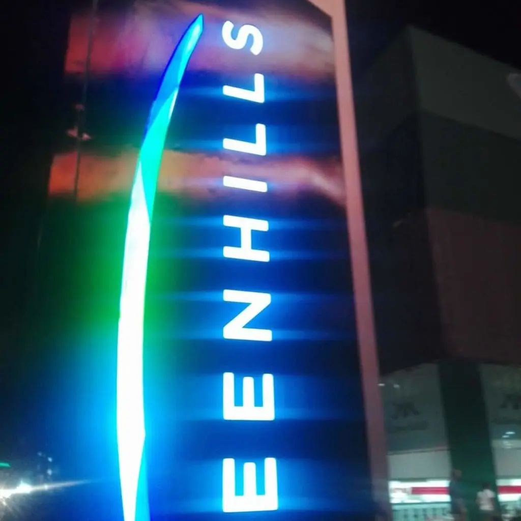 Outdoor building signage for GREENHILLS in bright blue, San Juan skyline at night, by M&G Global Ads.
