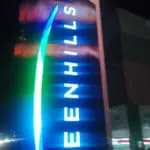 Outdoor building signage for GREENHILLS in bright blue, San Juan skyline at night, by M&G Global Ads.