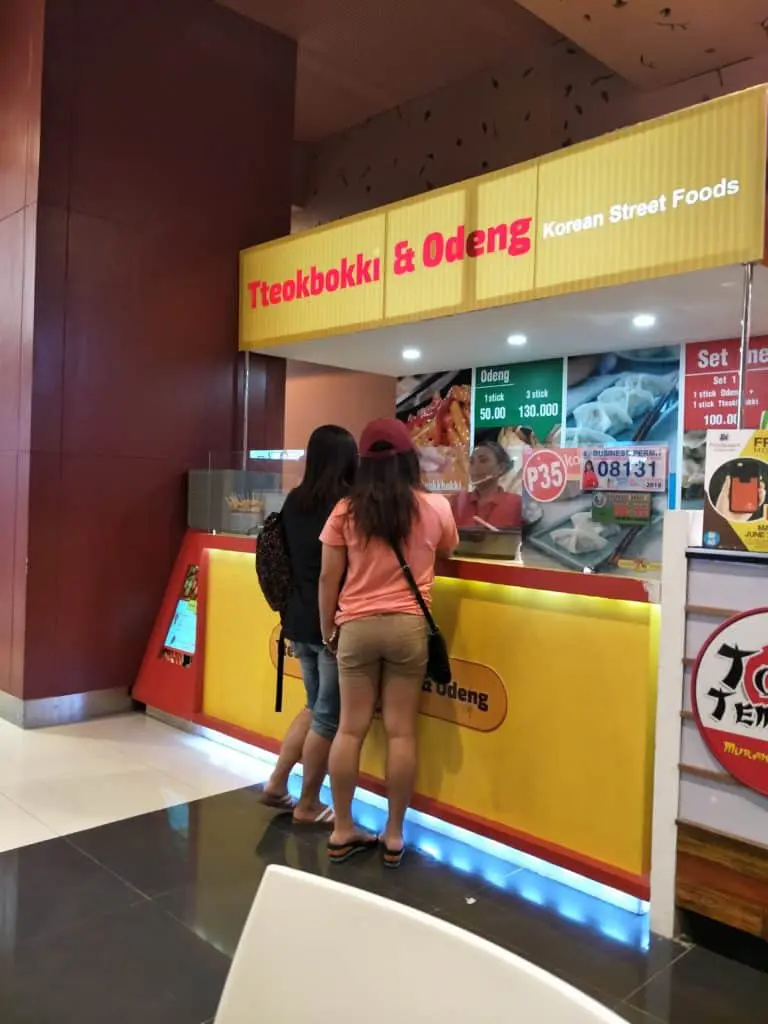 Two women at a Tteokbokki & Odeng stall with yellow and red LED signage in Quezon City by M&G Global Ads.