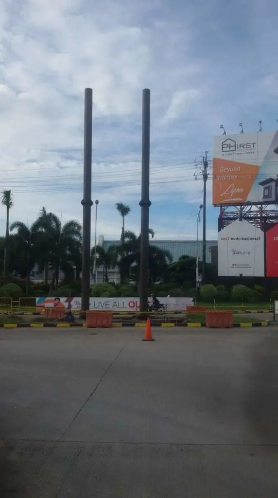 Building pylon signage and billboards in Makati street with poles, palm trees, cones, and sky by M&G Global Ads.