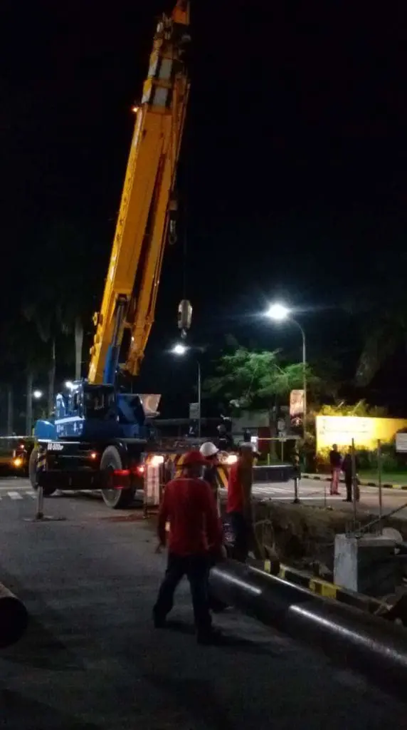 Nighttime construction in BGC with backlit outdoor signage, yellow crane, workers and barriers by M&G Global Ads.
