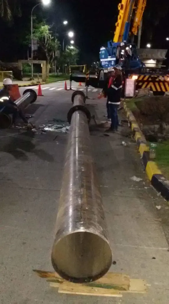 Workers at night install or repair a large road pylon sign in Quezon City with crane and cones, by M&G Global Ads.