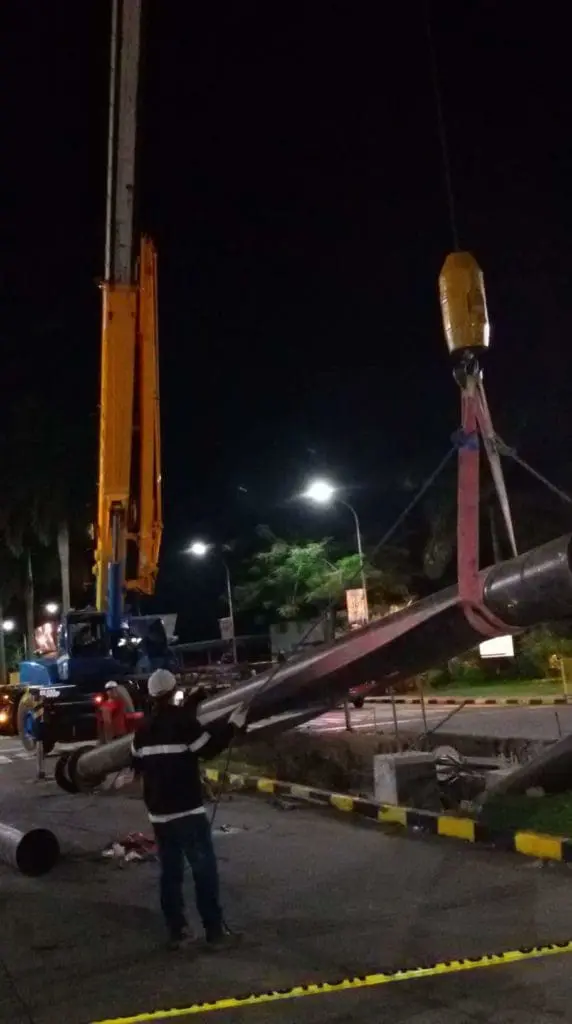 A construction worker near crane lifts pole at night with safety signage in Makati, area cordoned off, by M&G Global Ads.