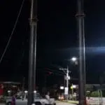 Construction workers by billboard sign in Mandaluyong at night, pickup truck parked nearby, streetlights glowing by M&G Global Ads.