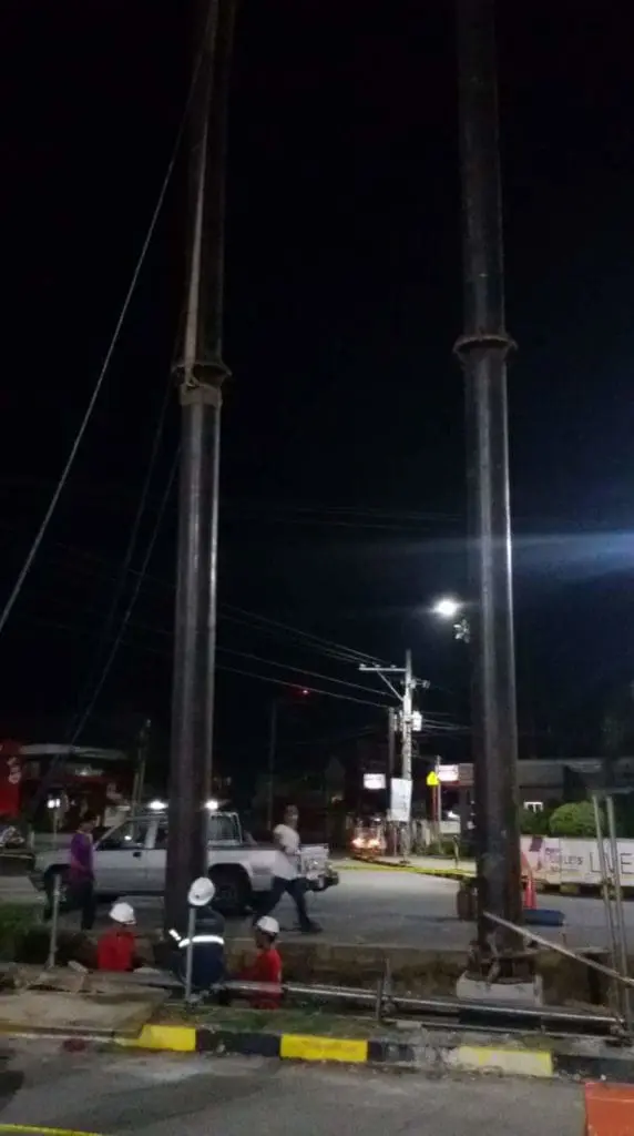 Construction workers by billboard sign in Mandaluyong at night, pickup truck parked nearby, streetlights glowing by M&G Global Ads.