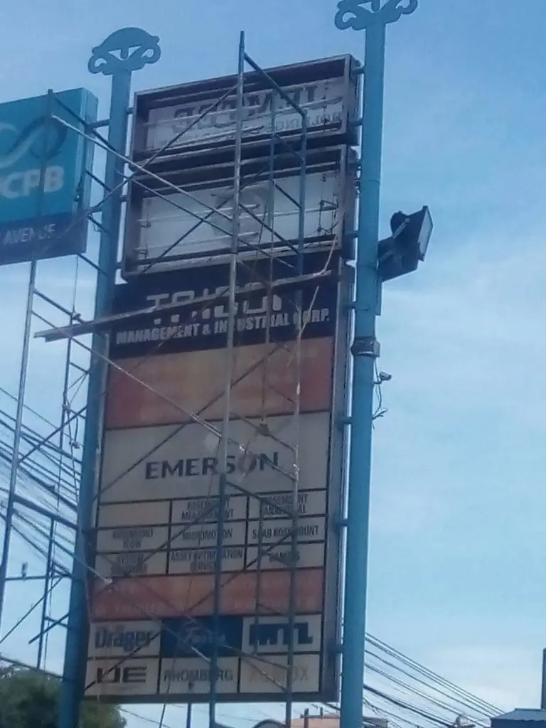 Pylon signage with multiple business names and scaffolding in Ortigas, blue sky and power lines. By M&G Global Ads.