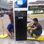 Pylon signage installation by three men in an outdoor parking lot in Makati, with cars and greenery in the background by M&G Global Ads.