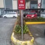 Parking lot speed limit sign 15 KPH in Makati, red and white metal signage by M&G Global Ads, cars and greenery in background.