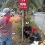 Building speed limit signage installation, 15 KPH, landscaped median in Quezon City by M&G Global Ads. Three men at work.