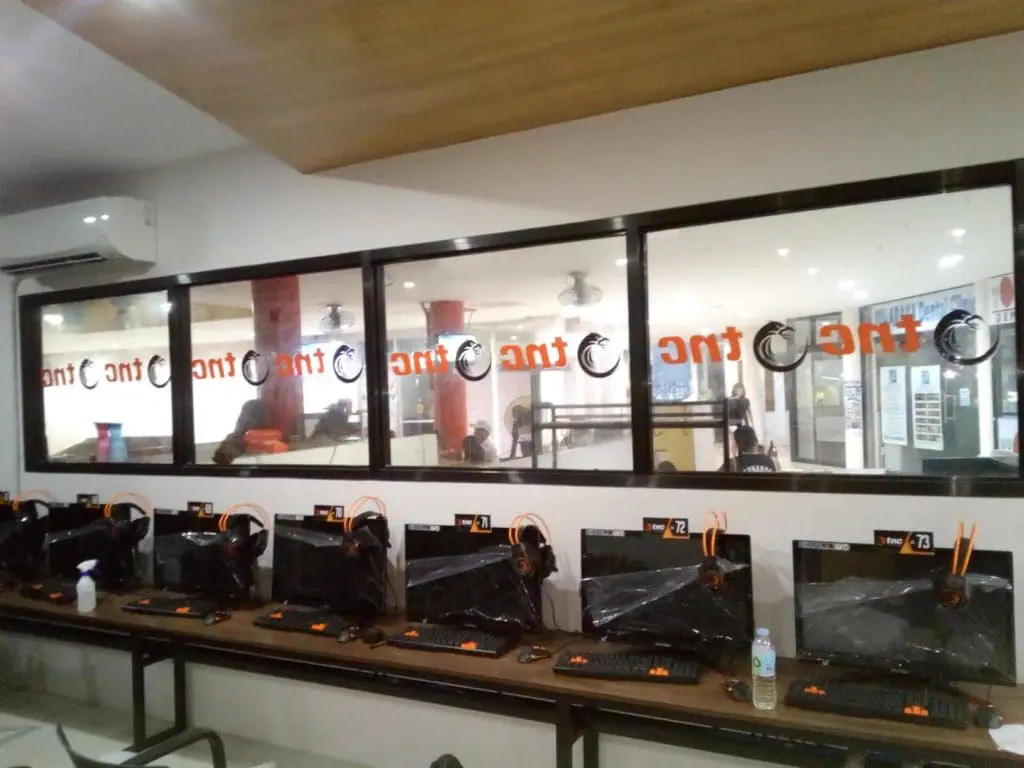 Indoor glass window signage for The One gaming cafe in Makati, featuring orange text; installed by M&G Global Ads.